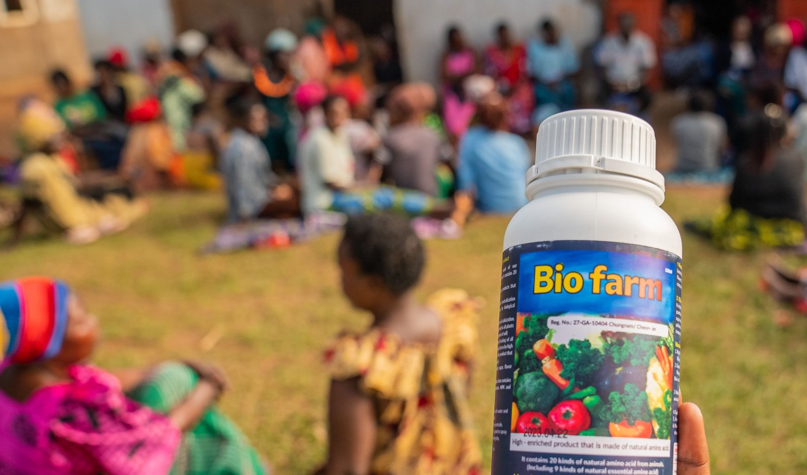 A bottle of Bio-Farm held up before a community farmer gathering in Uganda